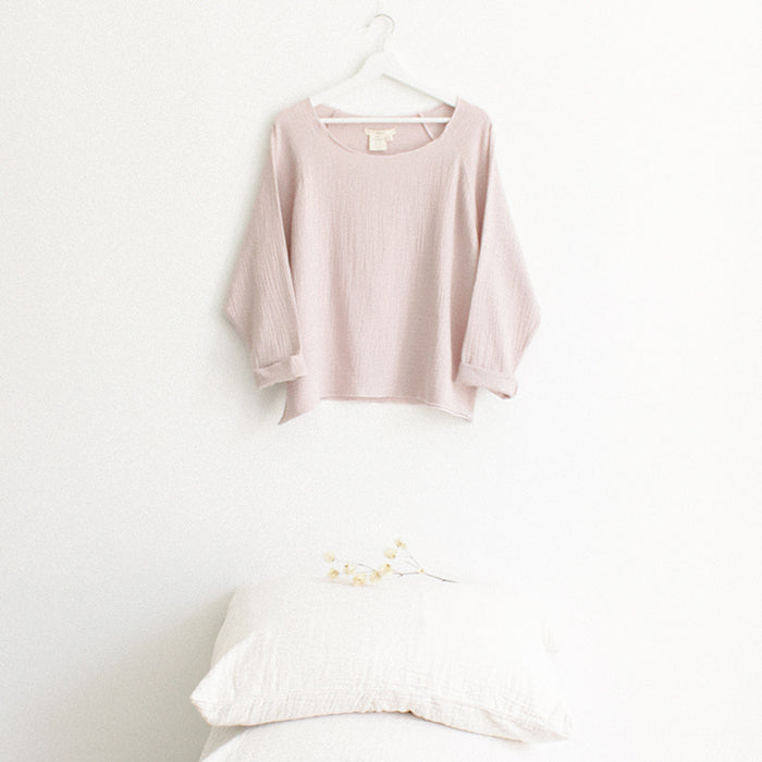 Red brown muslin shirt with cuffed long sleeves hanging above a stack of pillows.